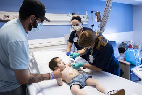 On 5 West, two nurses perform central line care to reduce the risk of CLABSI, while the patient’s father offers comfort