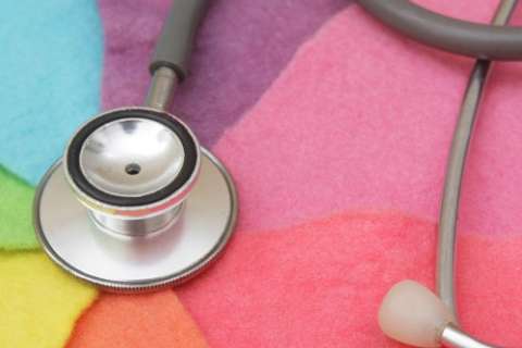 A close-up of a stethoscope's diaphragm and tubing resting on a brightly colored, textured background of pink, yellow, purple, and green fabric.