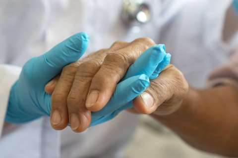 Close-up of a healthcare professional wearing blue gloves gently holding the hand of another person, symbolizing care and support.