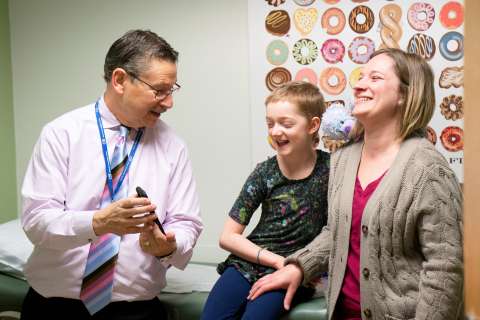 A doctor talks with a smiling child and a woman in a medical office.