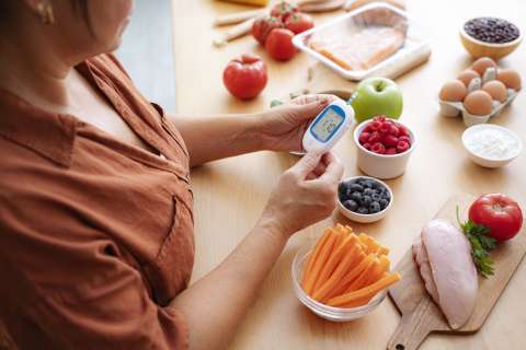 Person checking blood glucose with meter beside berries, carrots, eggs, and turkey
