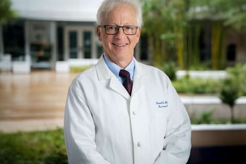 Dr. Daniel Lo in white coat and tie smiling in hospital courtyard.