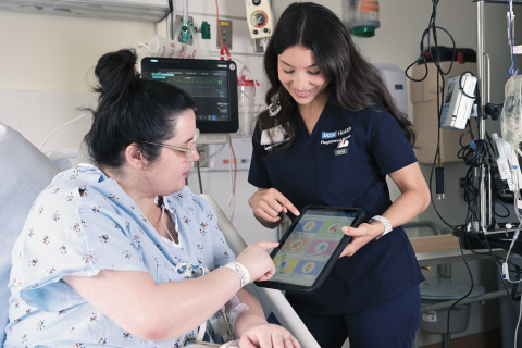 Nurse assisting a patient with a tablet in a hospital room.