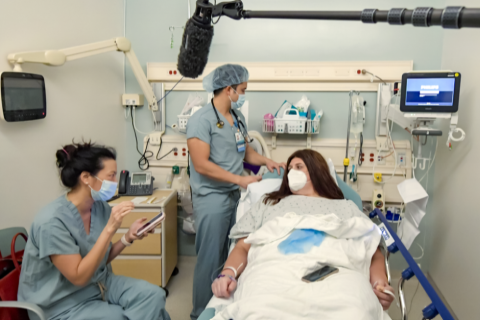 two medical professionals assisting a female patient laying in a gurney.