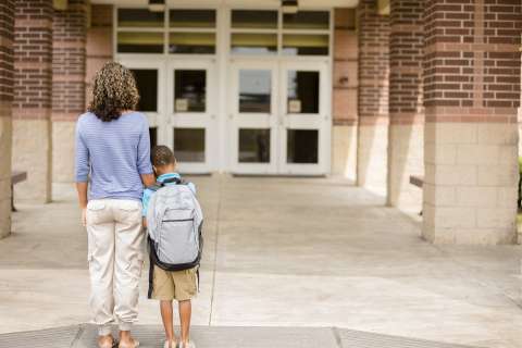 Adult holding child's hand walking toward a school entrance