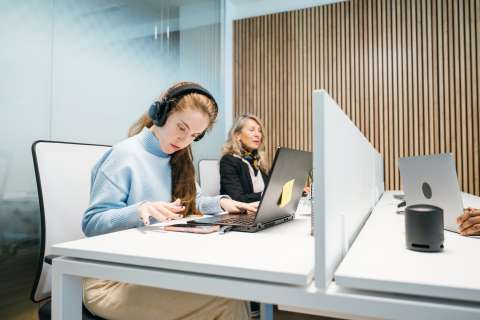 A young woman with cerebral palsy types on her smartphone while sitting at a white desk in an office.