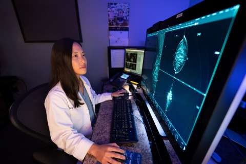 Dr. Tiffany Yu at workstation reviewing medical scans on large monitors.
