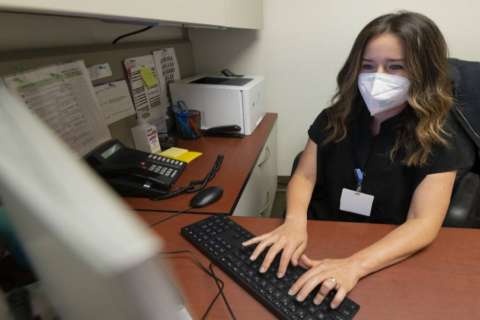 Rachel Frankenthal at a desk typing on a keyboard with monitor and phone visible