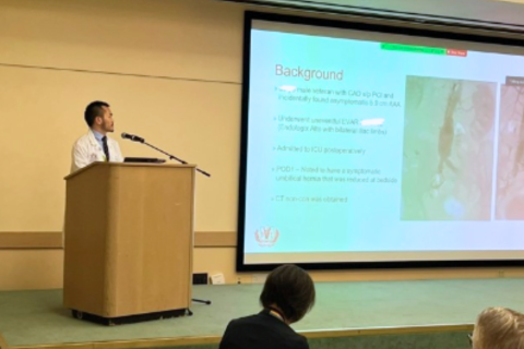 CORELAB Visiting Researcher presentation. A doctor on a podium presenting a slideshow on a big screen.