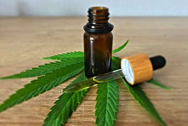 A cannabis tincture bottle and pipet sits atop a cannabis leaf on a wooden table.