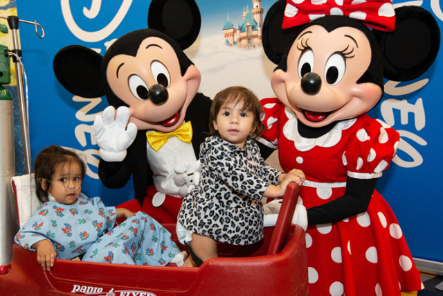 Two children in a wagon posing with Mickey and Minnie mouse at a Disney UCLA event.