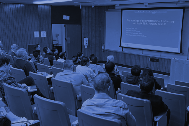  A lecture hall filled with people attending a presentation titled "The Marriage of dualPortal Spinal Endoscopy and OLIF: Amplify dualLIF".