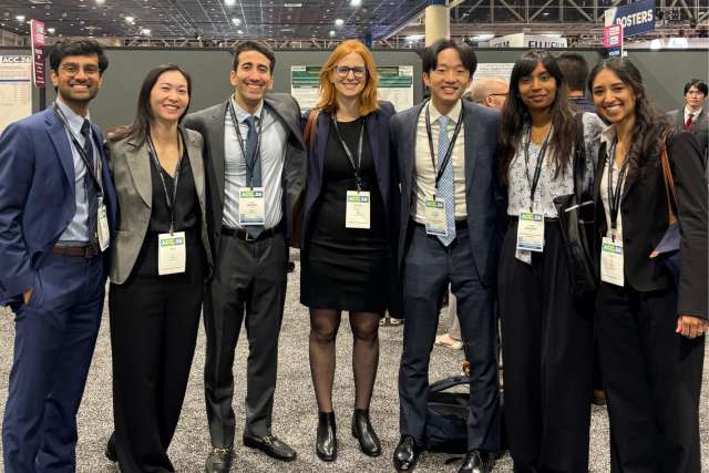 Eight professionals in business attire wearing conference badges, standing and smiling.