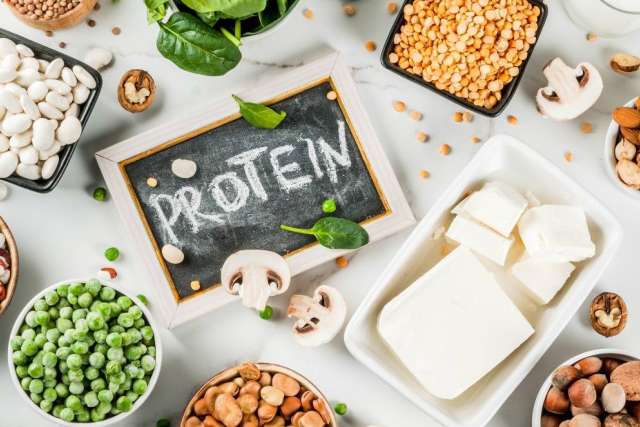 Assorted protein foods (beans, nuts, tofu, peas) around chalkboard "PROTEIN."