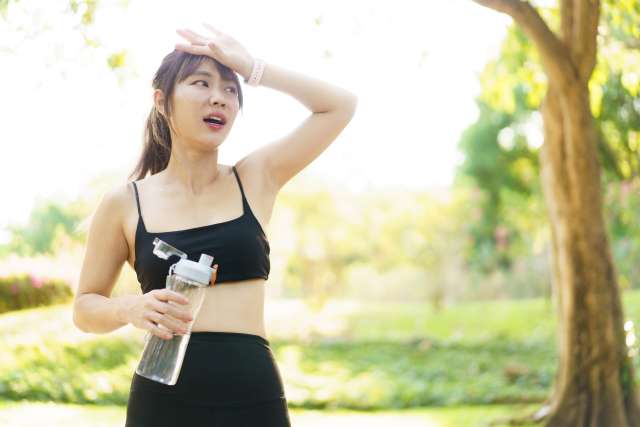 Woman in workout clothes holding water bottle wiping her forehead outdoors