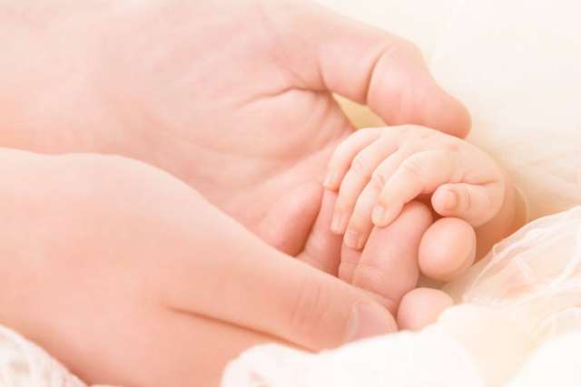 A close-up of an adult hand gently holding a small baby's hand.