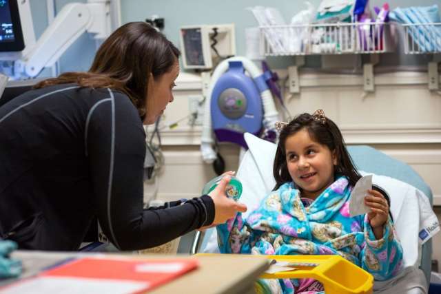 Karleen Wray leaning over, speaking to six year old patient who is lying in hospital bed