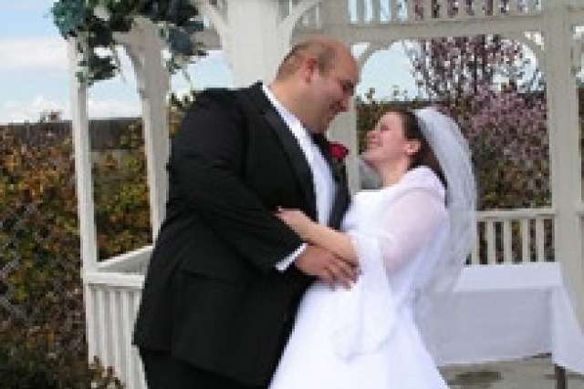 A couple dressed in formal wedding attire standing under a white gazebo, surrounded by outdoor foliage and floral decorations. Provide your feedback on BizChat