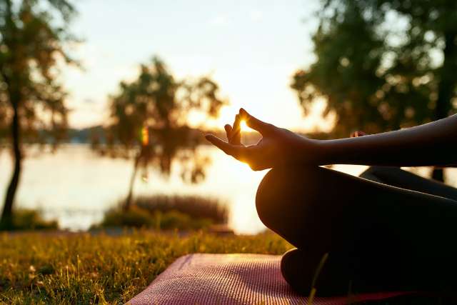 Woman Meditating by the Beach with Sun in Background