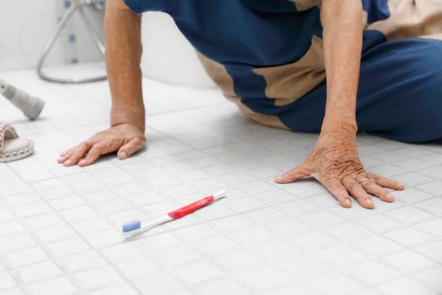 Hands of person on tiled bathroom floor next to toothbrush.