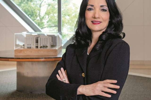 Johnese Spisso stands with her arms crossed, wearing a black blazer. Her relaxed pose suggests she is approachable and confident.