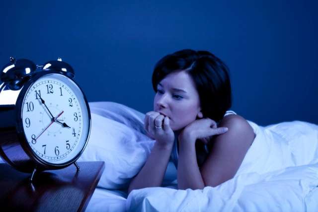 Woman awake in bed watching alarm clock