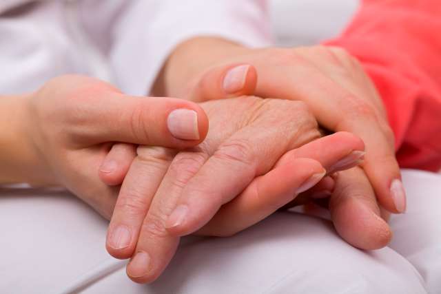 Caregiver holding elderly patients hand at home