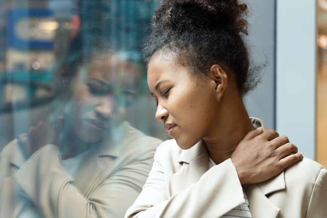 Woman at window holding shoulder in pain
