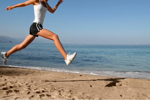 woman in black shorts, white shirt, and shoes, running on the beach