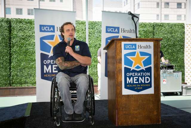 A man in a wheelchair speaks at a podium with "Operation Mend" branding.
