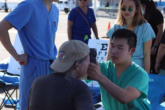 Fam Care Village volunteer checks a man's eye at an outdoor health booth