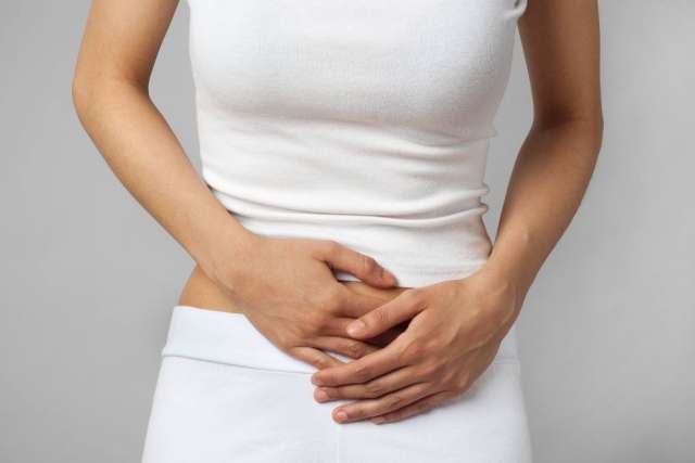 A close-up of a person wearing white clothing, gripping their lower abdomen, suggesting abdominal pain or discomfort.