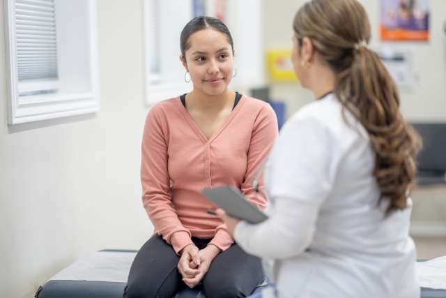Woman on exam table speaking with clinician holding a tablet