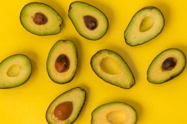 Halved avocados, some with pits, arranged on yellow background.