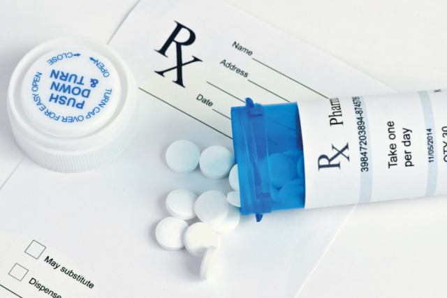 a blue prescription bottle opened on a table with white circular pills spilling out of it, on top of a white prescription paper