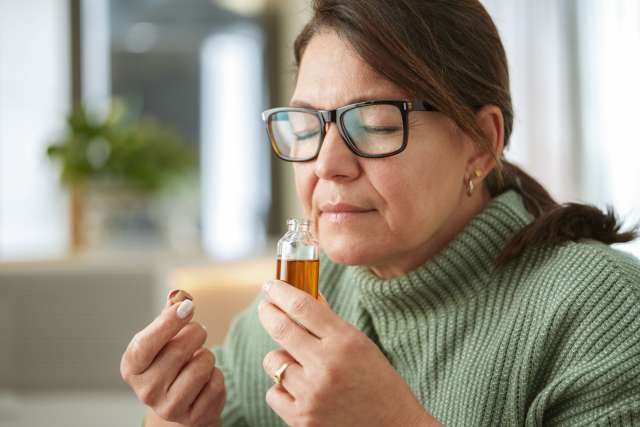 Woman with glasses smelling perfume from a small glass bottle