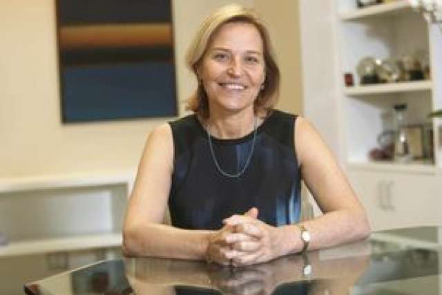 A person seated at a table, wearing a sleeveless black top and a necklace.