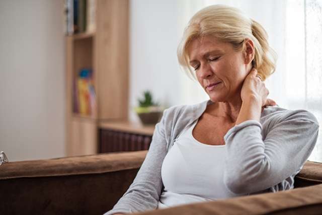 A woman sitting on a sofa, looking thoughtfully while touching her neck.