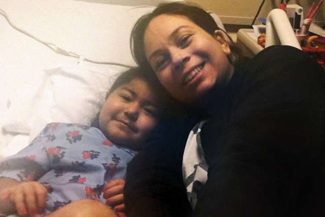 Mother and daughter, Giorgiana and Giuliana, smiling together in a hospital bed. Giuliana is a young girl with long, dark hair.
