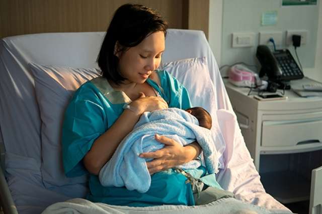 Mother nursing newborn in hospital bed.
