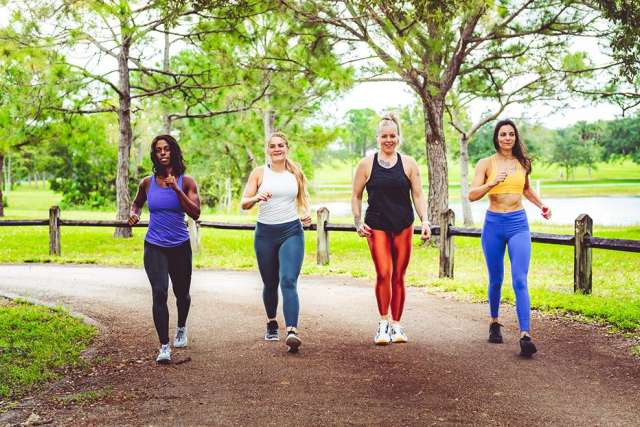 Four women walking together on a tree-lined park path