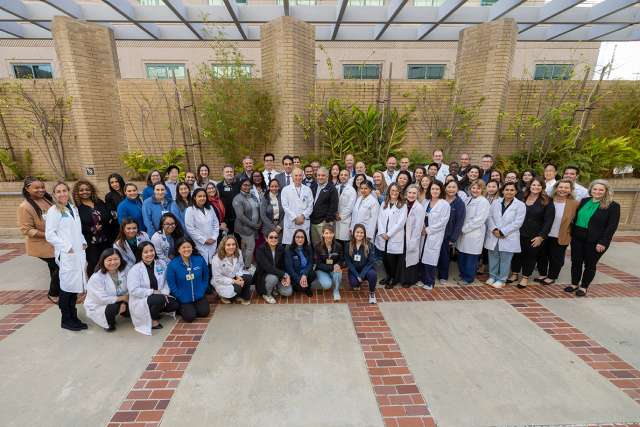Group photo of diverse medical professionals in white coats outside.