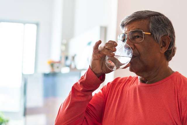 Older man in red sweater drinking water from a glass