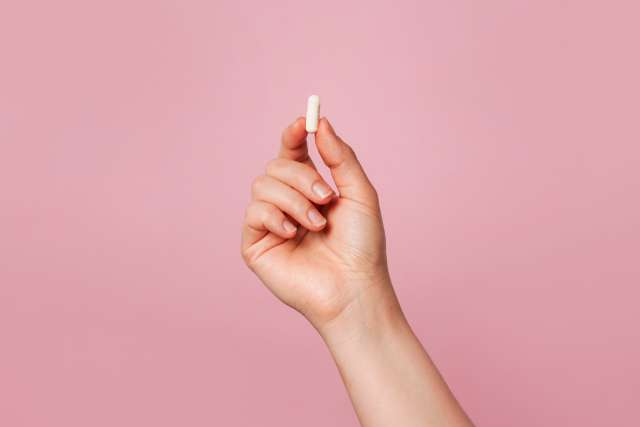 Hand holding small white pill against pink background.
