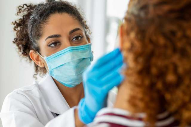 Masked clinician examining a patient's throat