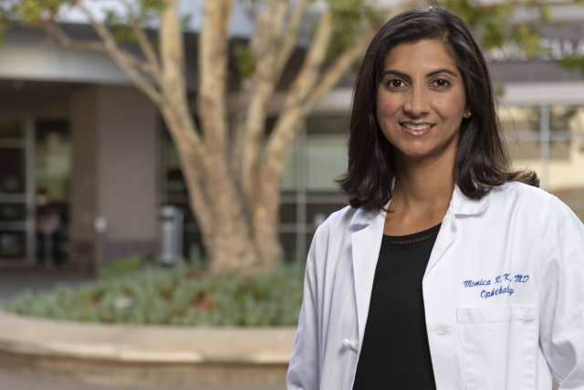 Monica Khitri wearing a white lab coat and standing outside smiling