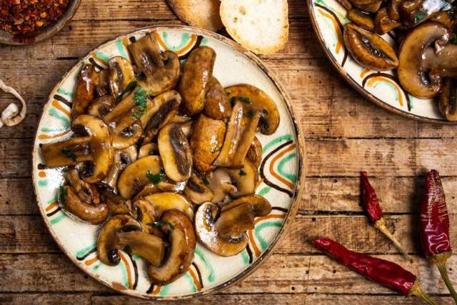 A rustic wooden table featuring an arrangement of fresh mushrooms and slices of bread.