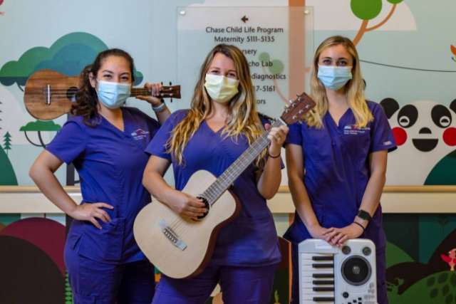 Three music therapists wearing masks stand in front of a colorful wall mural.