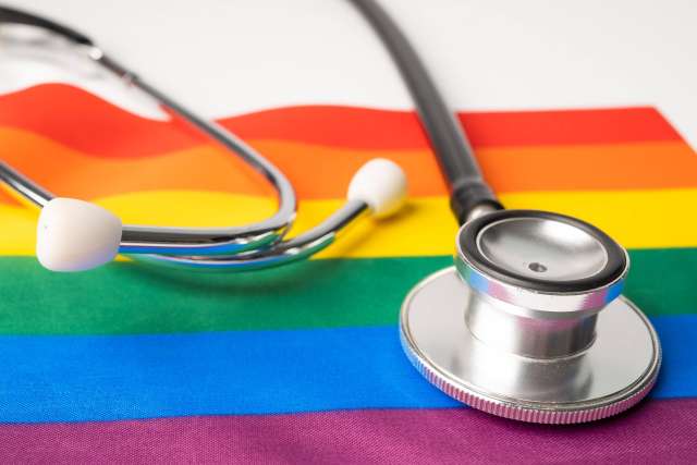 A close-up shot of a silver stethoscope lying on top of a vibrant Rainbow Pride Flag, symbolizing healthcare advocacy for the LGBTQ+ community.