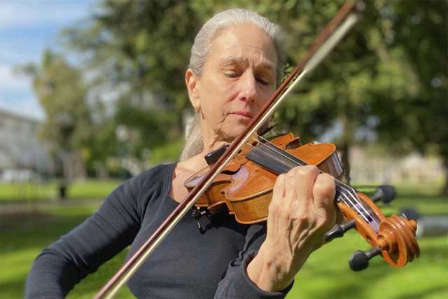 Constance Meyer, a veteran session musician, playing a violin on the grass.